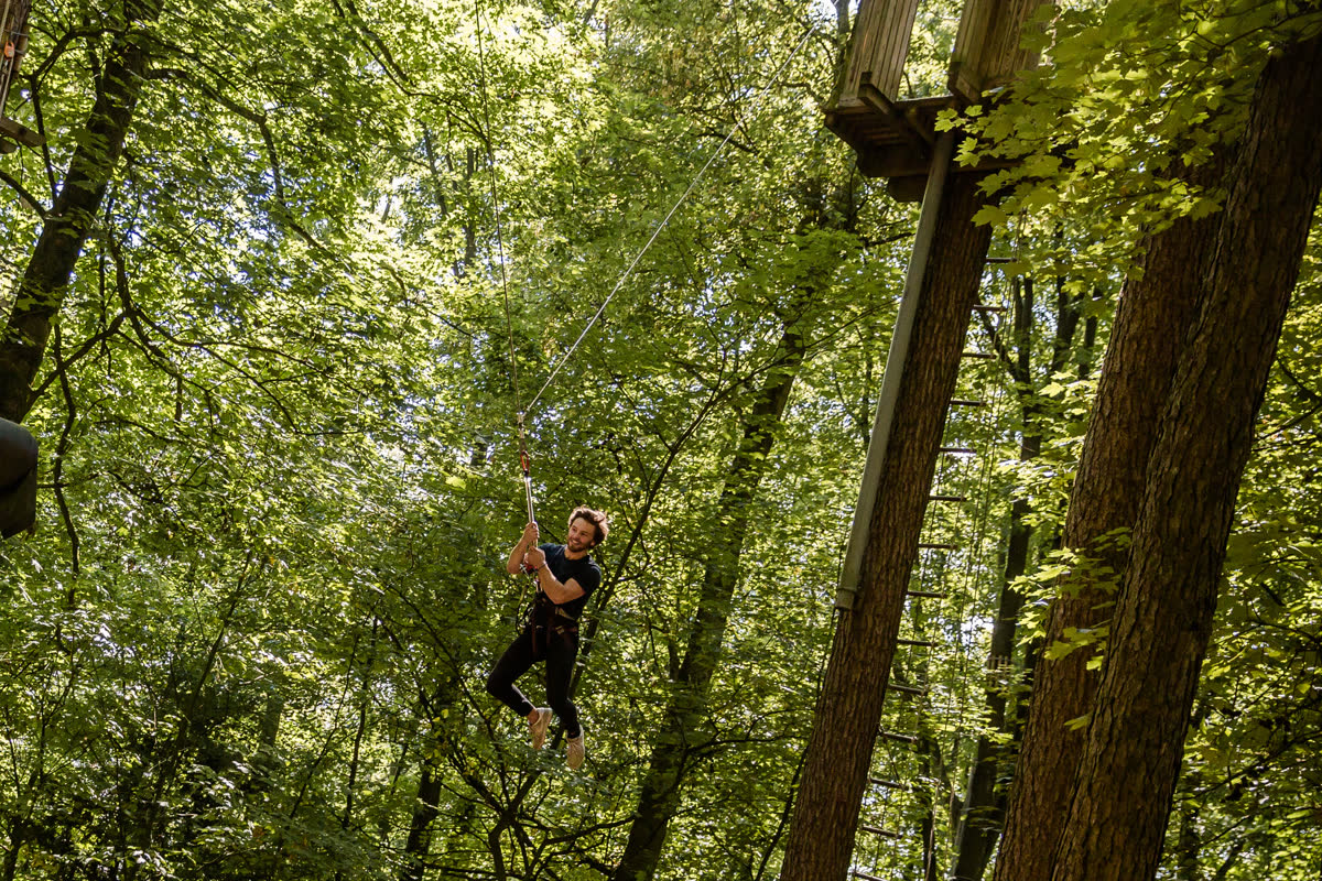 Person in free fall on the Big Swing, surrounded by tall trees